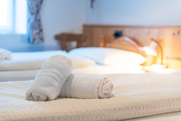 A neatly made bed with two rolled white towels and a bedside lamp.