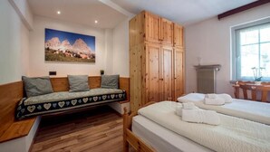 Un dormitorio con cama de madera, un banco de madera con cojines, un radiador y una ventana con vistas a montañas.