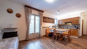 Un'accogliente stanza con un letto, un tavolo da pranzo con sedie, un angolo cottura con mobili in legno e una finestra con tende.