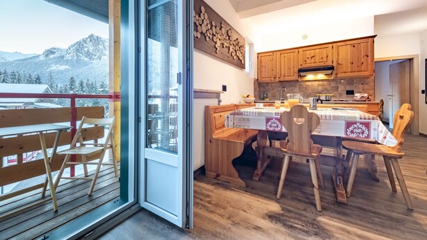 Una cucina moderna con mobili in legno, un tavolo da pranzo con sedie e vista su montagne innevate attraverso una porta in vetro.