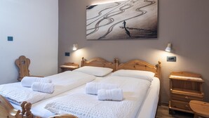 Un letto matrimoniale con lenzuola e asciugamani bianchi, una testiera in legno, comodini con lampade e un quadro astratto appeso al muro.