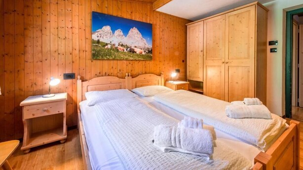 Une chambre aux murs lambrissés, comprenant deux lits, une table de chevet et une armoire.