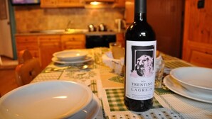 Une bouteille de vin Trentino Lagrein, millésime 2014, est posée sur une table avec des assiettes, et une télévision est visible dans une cuisine.
