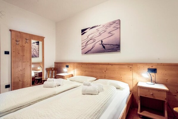 A hotel room with a large bed, wooden headboard, two bedside tables with lamps, a wooden wardrobe, and a wall-mounted abstract painting. - Apartment with 2 bedrooms and 3 bathrooms for 4-6 people in Val di Fassa (Sèn Jan di Fassa)