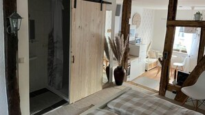 A modern interior with a sliding door leading to a bathroom, a large vase with dried plants, and a dining area with white chairs.