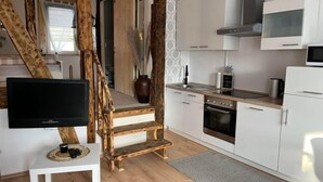 A modern kitchen with white cabinets, a stove, and a microwave. There is a wooden staircase leading to another room.