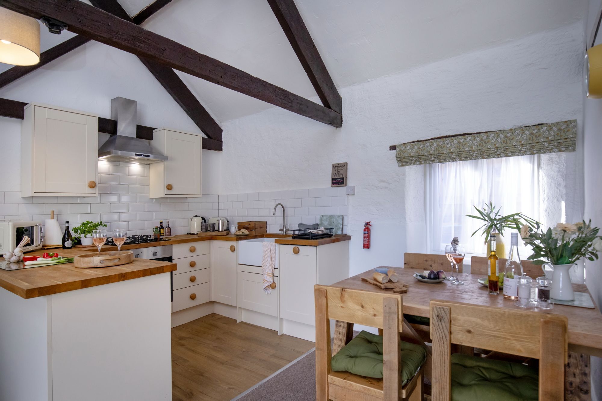 A kitchen with wooden beams, white cabinets, and a dining area with a wooden table and chairs.