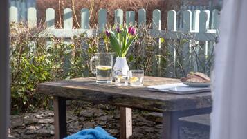Une table en bois, sur laquelle se trouvent un pichet en verre, deux verres, une assiette avec du pain et un vase rempli de fleurs.