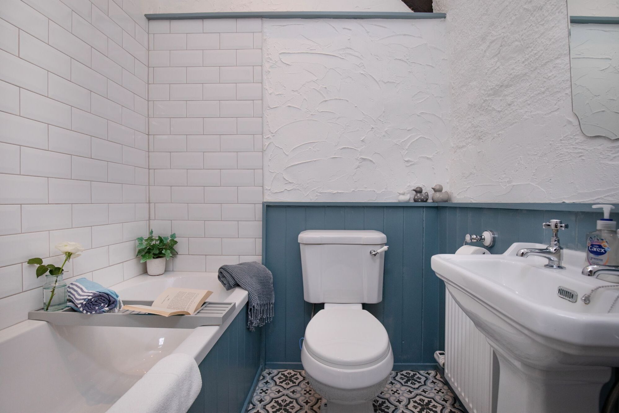 Une salle de bain avec des carreaux blancs, une baignoire, des toilettes et un lavabo.