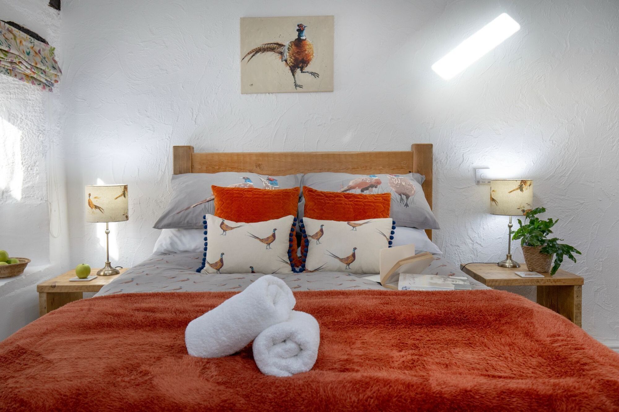 A neatly made bed with a red blanket and two white towels, flanked by pillows with bird patterns, and a wooden headboard.