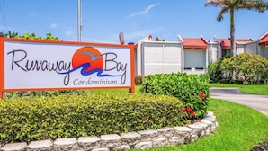 A sign for Ruwaway Bay Condominium with a clear view of the surrounding greenery and buildings.
