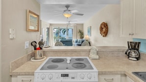 A kitchen with a gas stove, a ceiling fan, and a view to a living area.