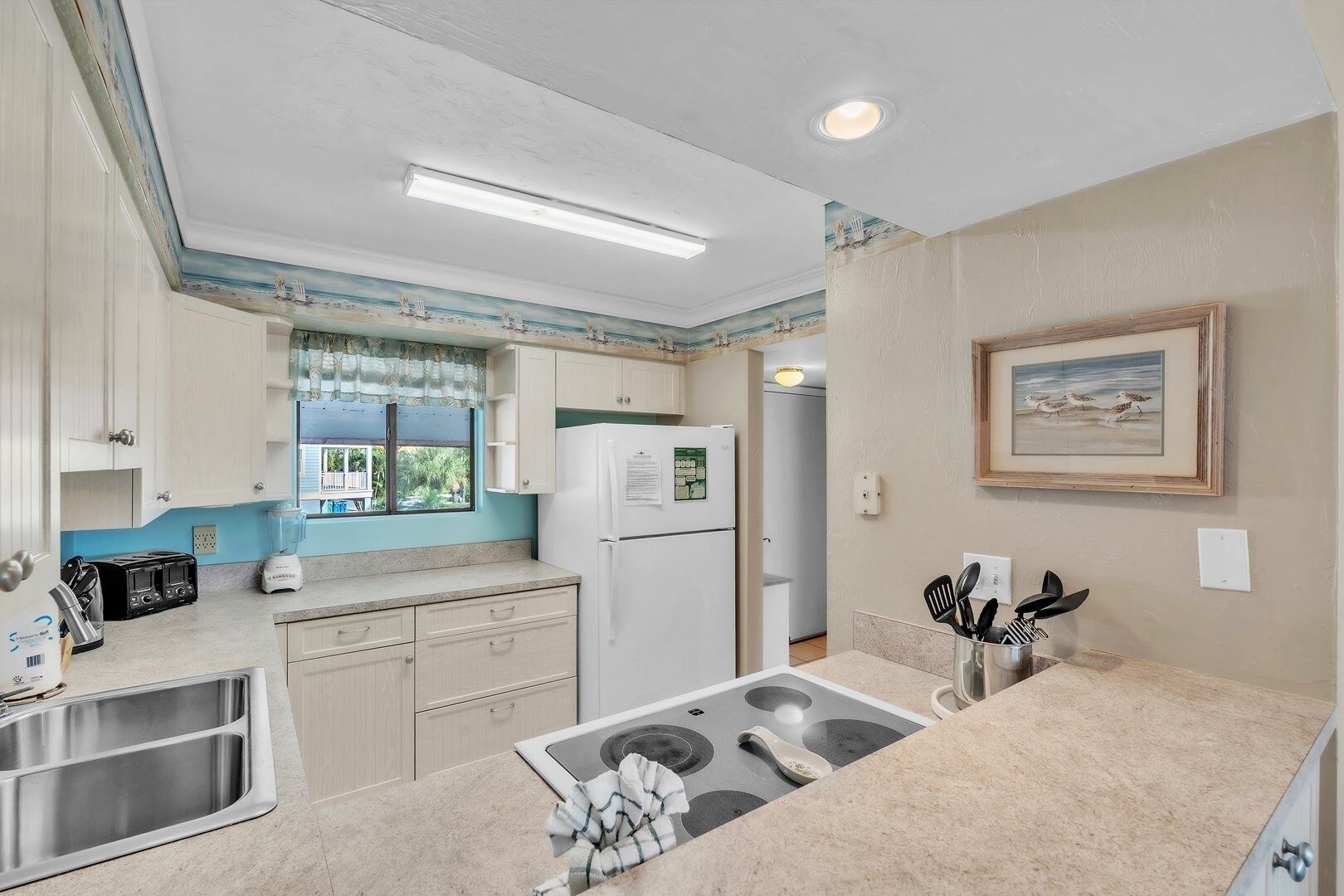 A compact kitchen with a refrigerator, a sink, a stove, and a window with a view of the outdoors.
