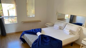 Une chambre d’hôtel comprenant un lit, une table de chevet, une commode, une fenêtre avec des rideaux et un miroir au-dessus du lit.