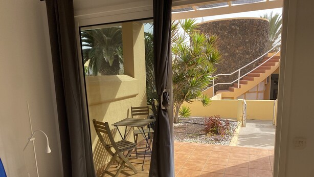 Une pièce dotée d’une porte-fenêtre coulissante donnant sur un espace extérieur comprenant une terrasse, une petite table avec des chaises et un escalier.