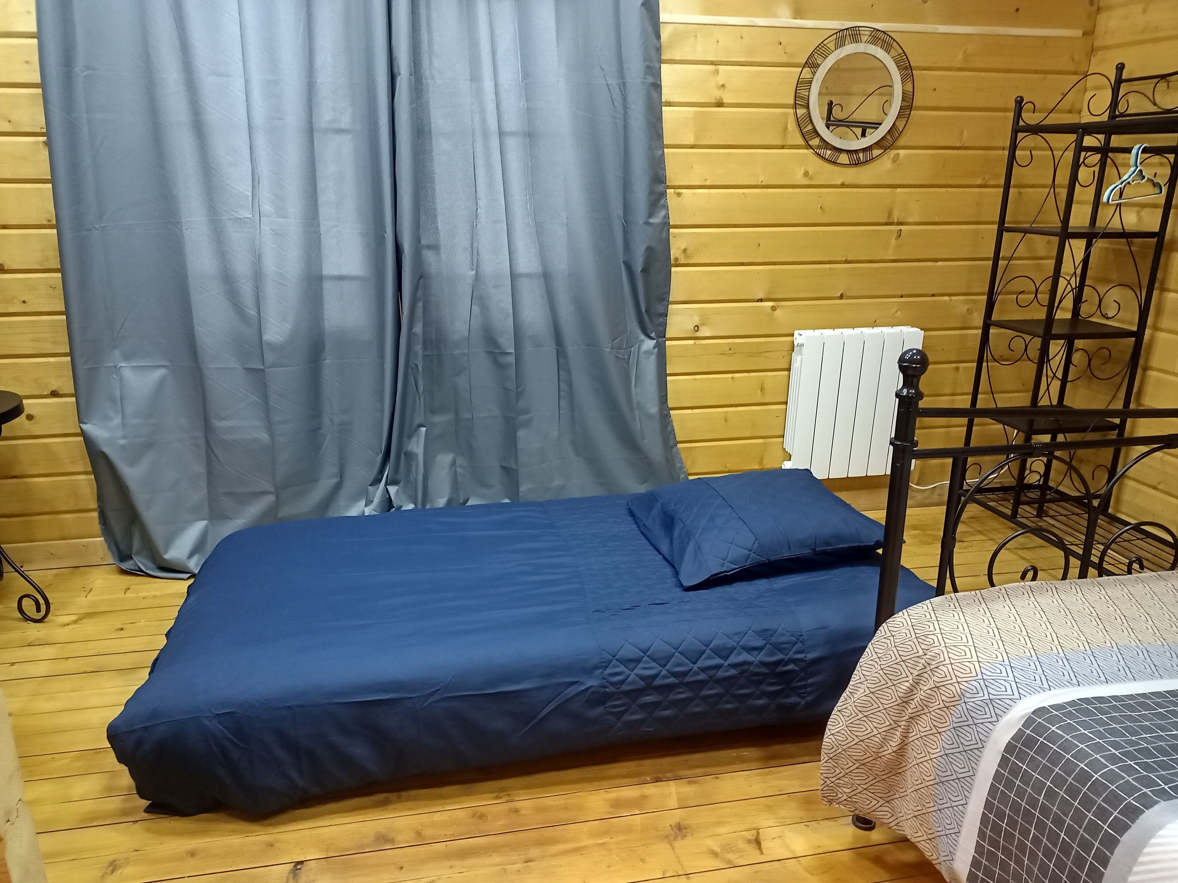 Ein Zimmer mit einem Bett, einem Vorhang, einem Heizkörper und einem Metallgestell.