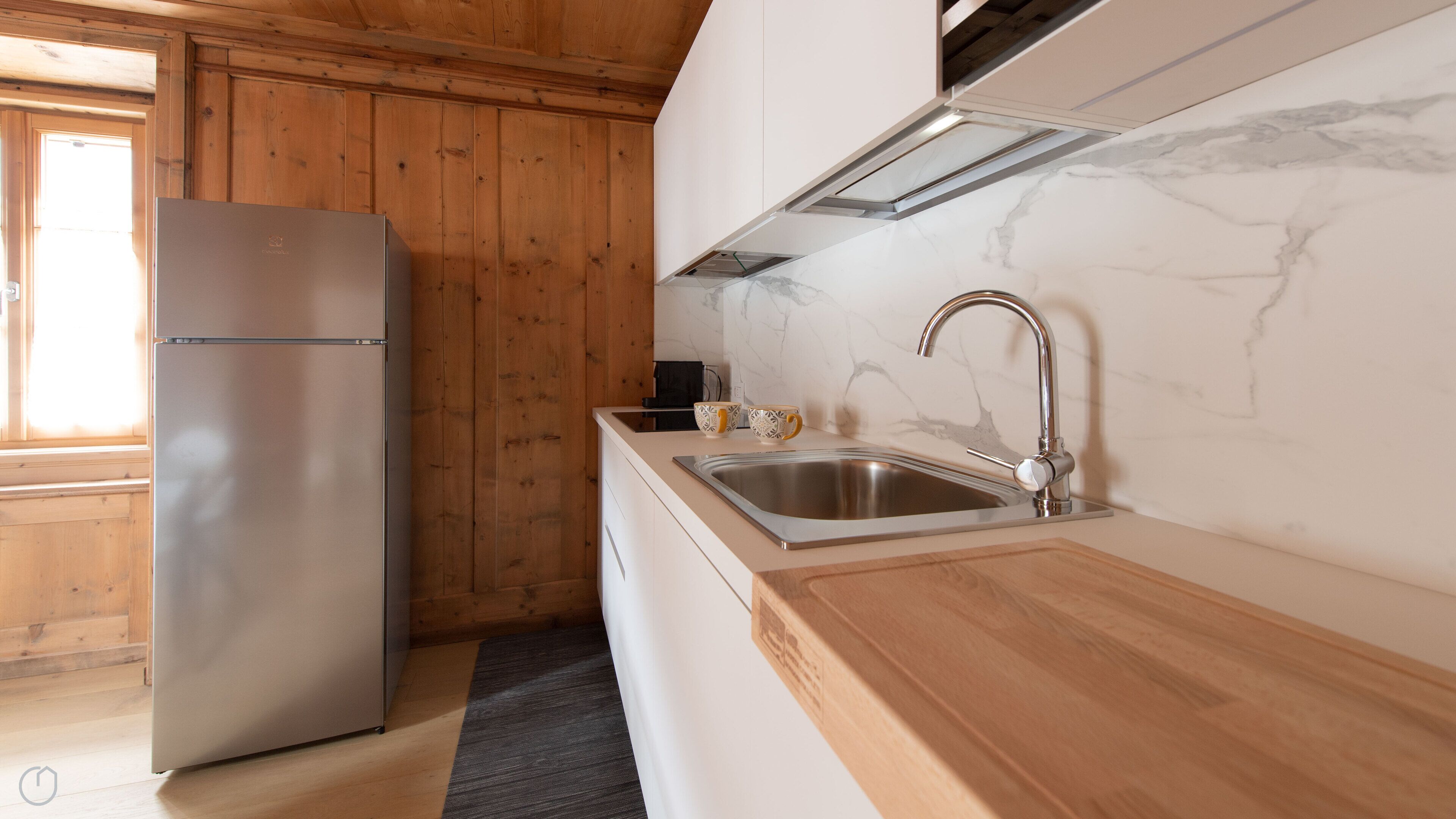 A modern kitchen with a stainless steel refrigerator, a sink with a modern faucet, and wooden cabinetry.
