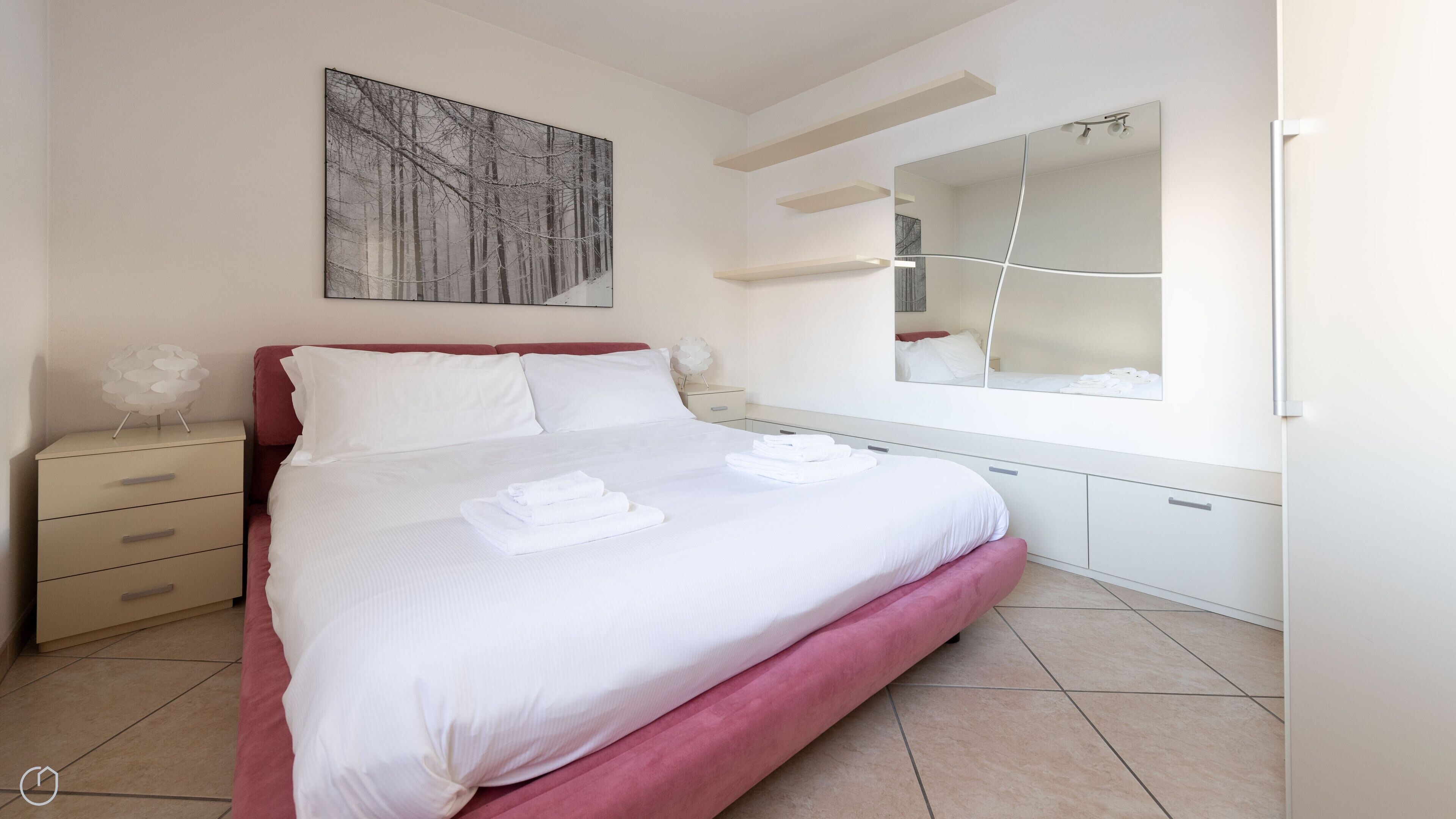 Un dormitori modern amb un llit gran, una tauleta de nit, una commode, un mirall i un quadre a la paret.