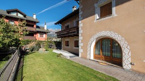 A residential property with a well-maintained lawn, a paved driveway, and a wooden door with an arched window. - Funivie 6A (Bormio)