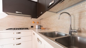 A modern kitchen with two stainless steel sinks, a gas stove, and dark cabinets.