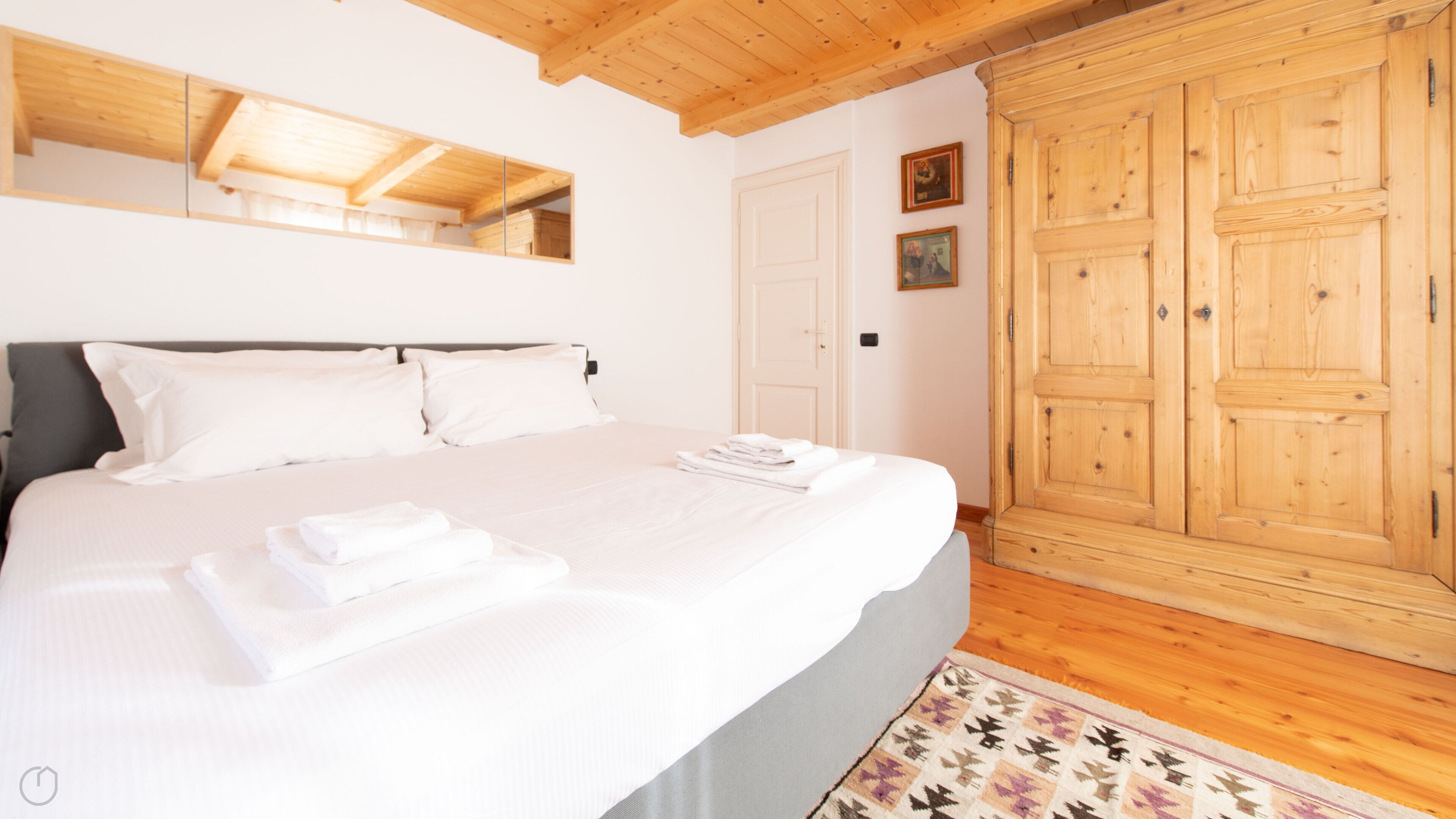 Un dormitorio con una cama grande, un armario de madera y un espejo sobre la cama.