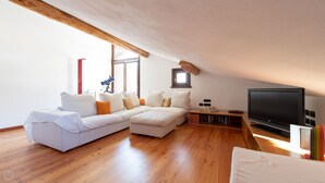 A modern living room with a sectional sofa, a flat-screen TV, wooden flooring, and a sloped ceiling. - Sertorelli 60 (Bormio)