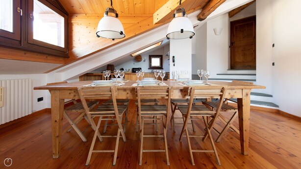 A spacious dining area with a long wooden table set for a meal, wooden chairs, and pendant lighting. - Sertorelli 60 (Bormio)