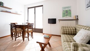 A living room with a dining table, chairs, a sofa, a coffee table, and a TV mounted on the wall. - Sertorelli 2 (Bormio)