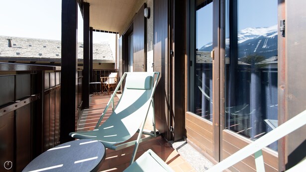 A balcony with a view of snow-capped mountains, a chair, and a table. - Sertorelli 2 (Bormio)