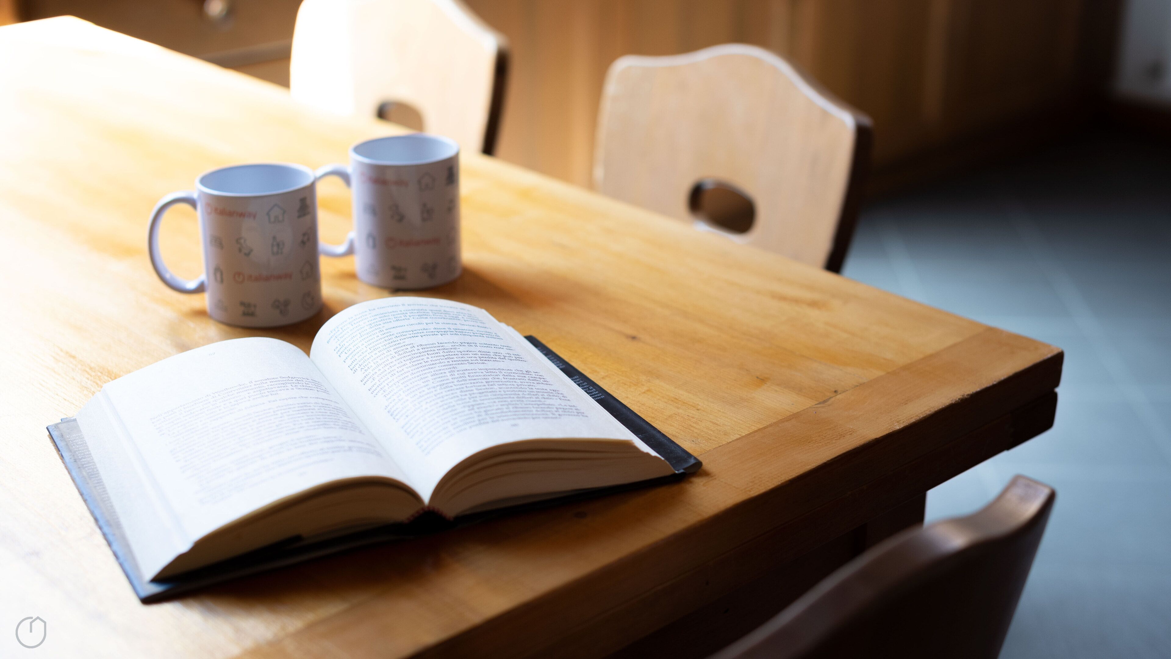 An open book on a wooden table with two mugs beside it.