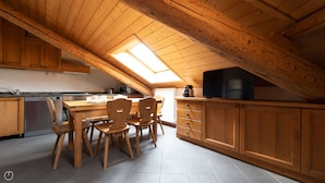 A kitchen with wooden cabinets, a dining table with chairs, a built-in oven, and a television on a wooden shelf. - Andreola 1 (Bormio)