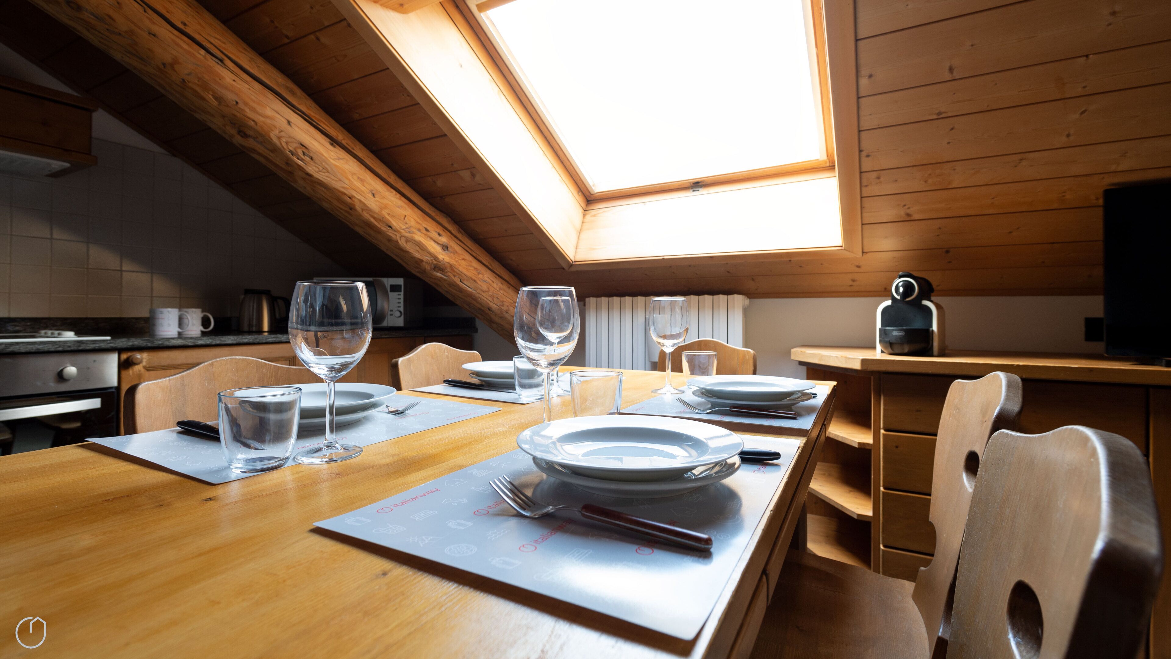 A dining area with a wooden table set for four, a skylight above, and wooden walls.