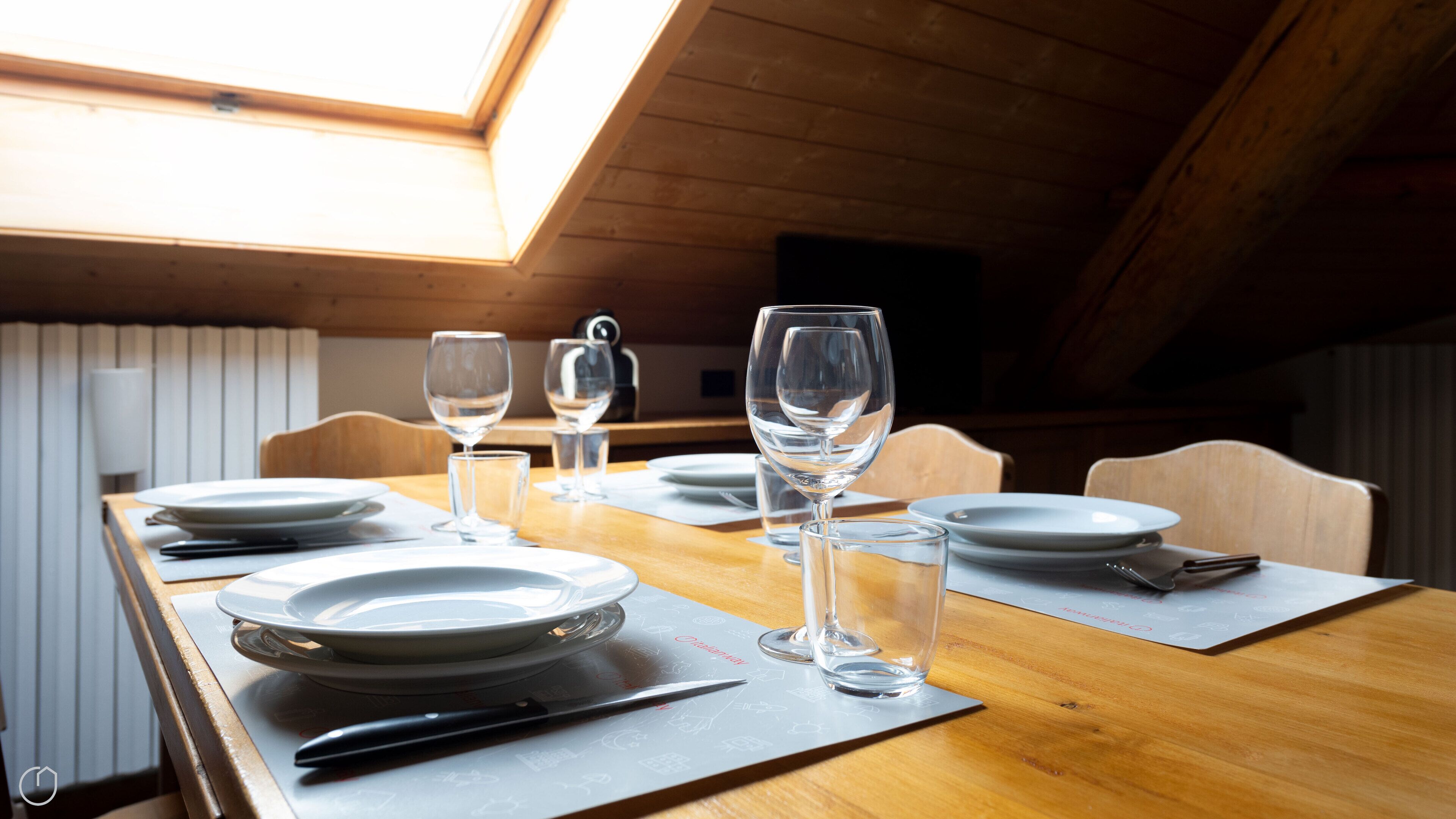 A dining table set with plates, glasses, and cutlery in a room with wooden walls and a sloped ceiling.