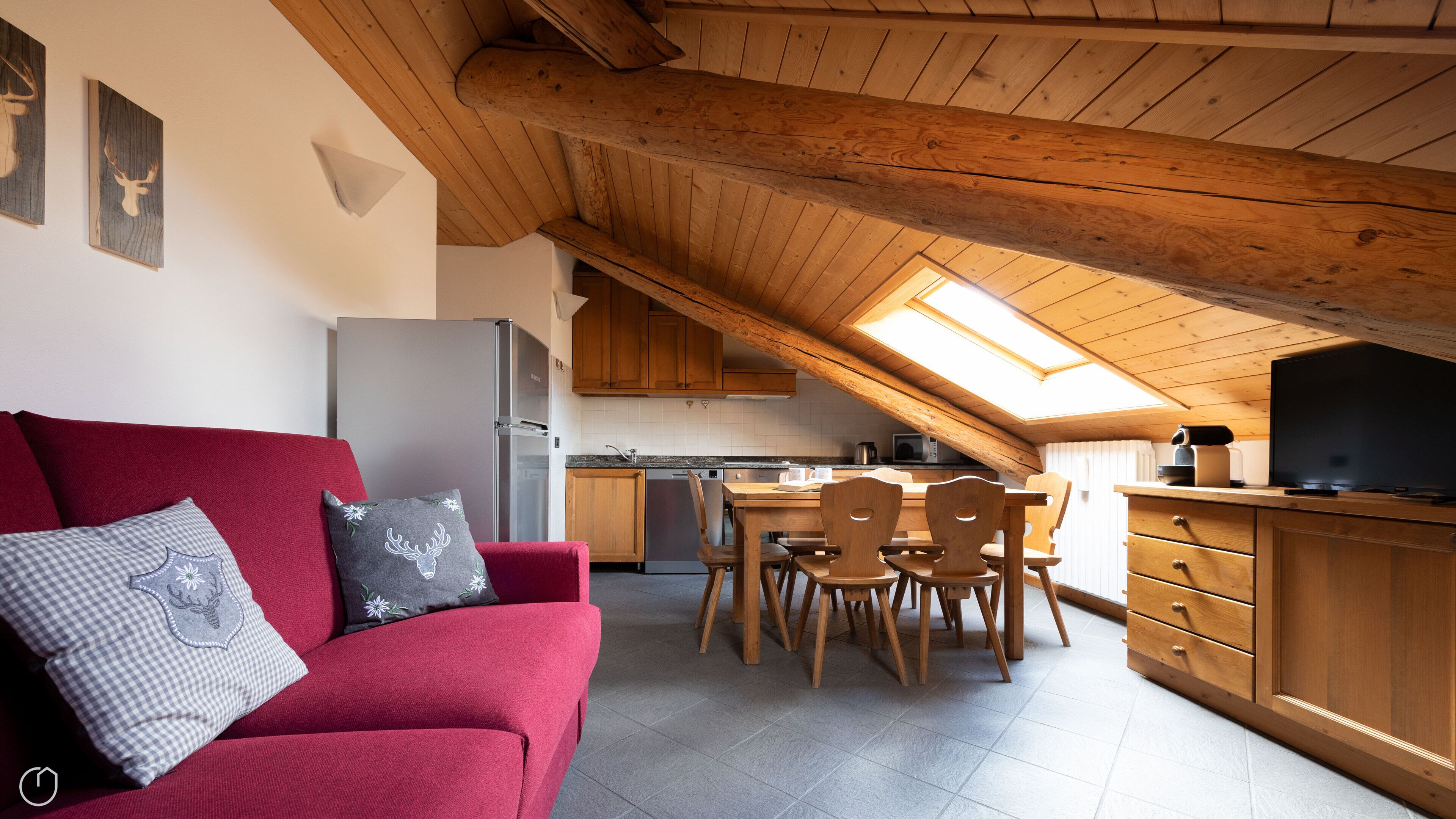 A cozy loft-style living space with a red sofa, wooden dining table, and kitchen area.