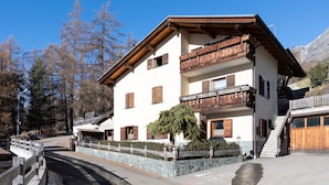 A multi-story building with wooden balconies, a stone wall, and a clear view of the surrounding trees and mountains.