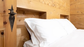 A wooden cabin room with a bed, a metal wall-mounted light fixture, and a wooden door.