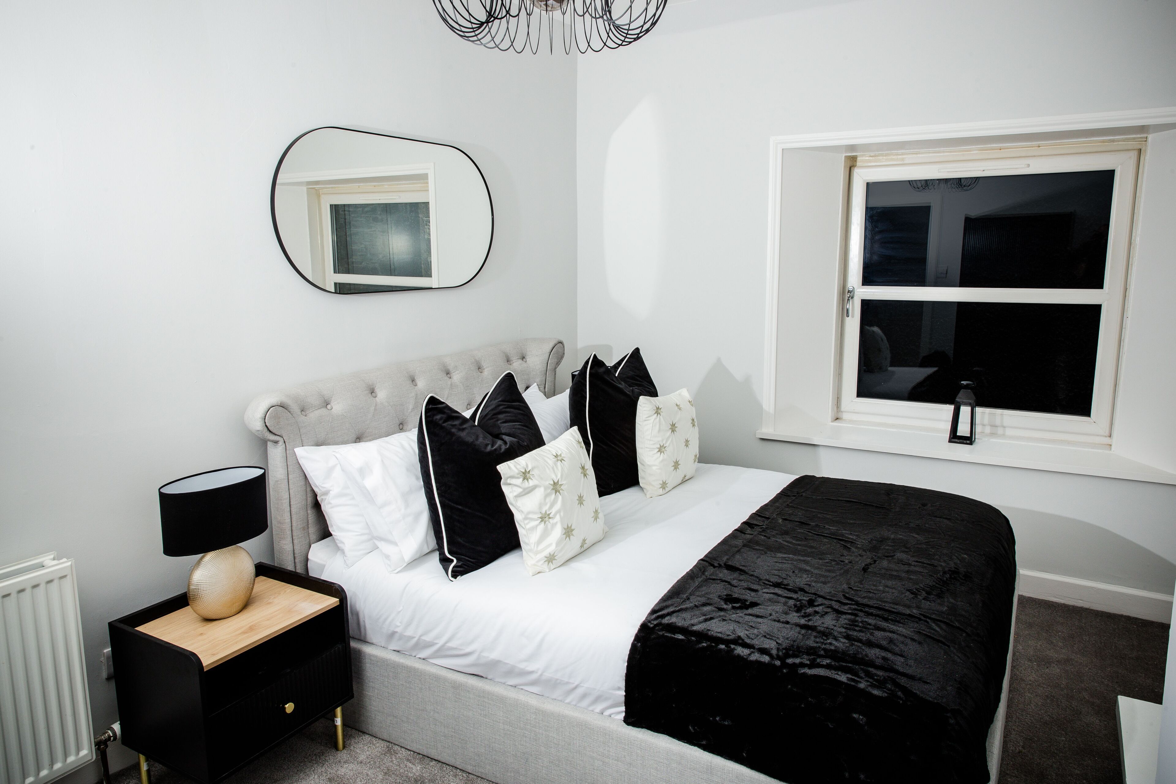 A bedroom with a bed, nightstand, lamp, and a window with a view.