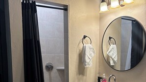A bathroom with a shower, a sink, a mirror, and a towel rack.