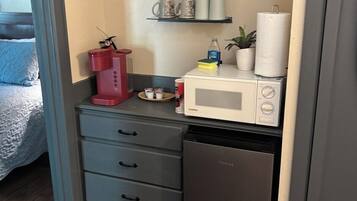 Une petite cuisine équipée d’un four à micro-ondes, d’un petit réfrigérateur et d’une machine à café. On y trouve également des étagères avec des tasses et une plante.