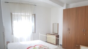 A bedroom with a bed, a dresser, a wardrobe, and a window with curtains. - Apartment among ancient olive trees a short distance from the excavations of Velia. Sea view (Ascea)