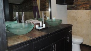 A bathroom with two glass bowl sinks, a large mirror, and a toilet.