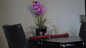 A dining table with a vase of purple flowers, a potted plant, and two red napkins.
