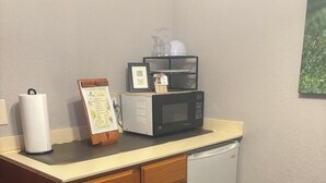 A small kitchenette with a microwave, a paper towel dispenser, and a menu board. - English Room at Whispering Pines Inn (Norman)
