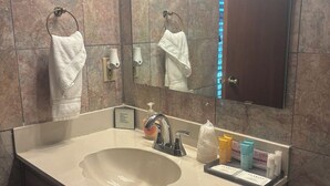 A bathroom with a large sink, a mirror, a towel rack, and toiletries. - English Room at Whispering Pines Inn (Norman)