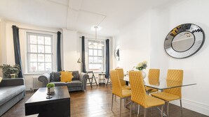 A modern living room with a sofa, coffee table, and dining area with chairs. - Marble Arch Apartments (London)
