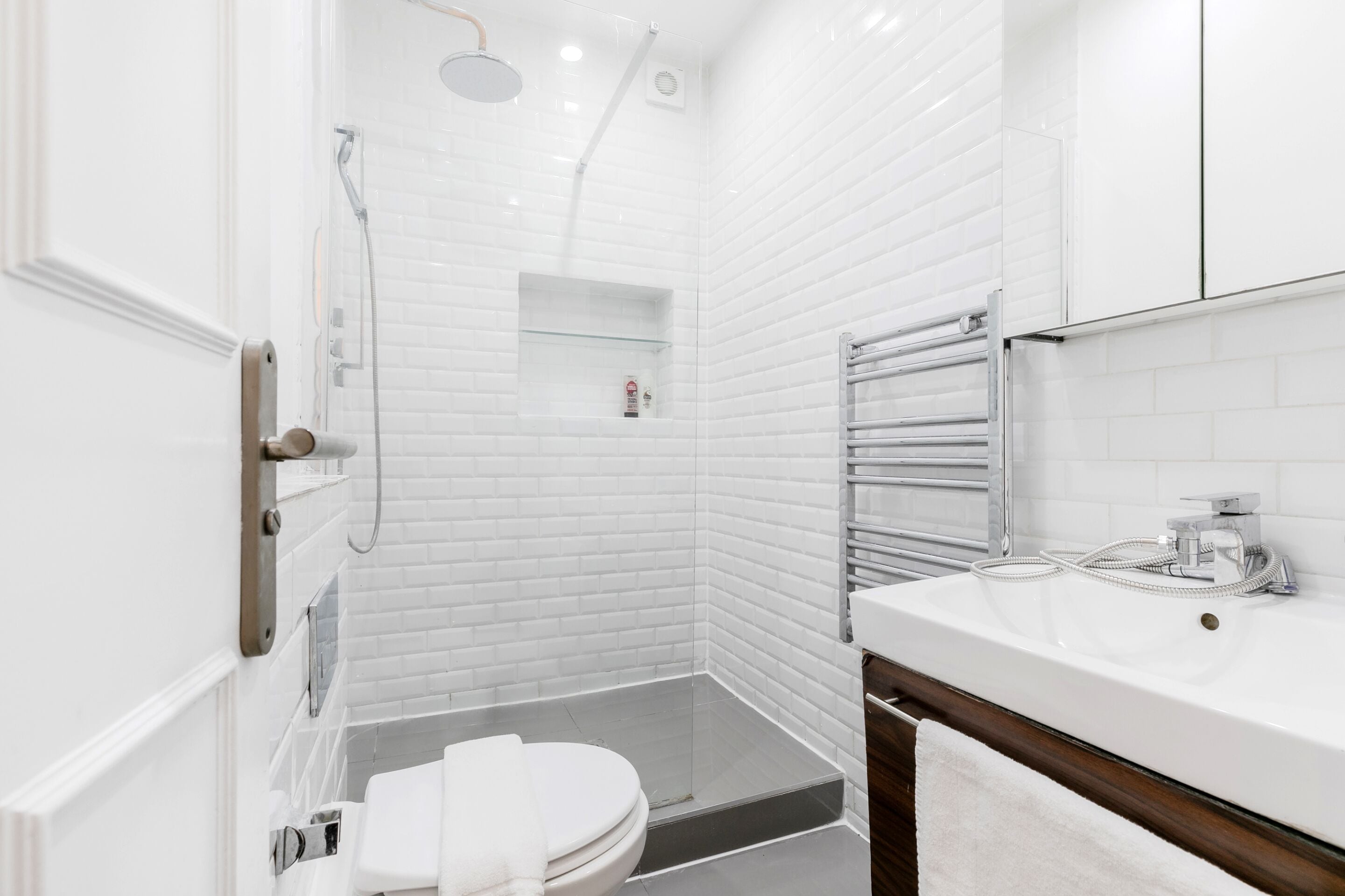 A modern bathroom with white subway tiles, a glass shower enclosure, a white toilet, and a wooden vanity with a mirror.