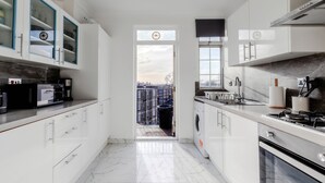 A modern kitchen with white cabinets, a built-in oven, and a view to the outside. - Marble Arch Apartments (London)