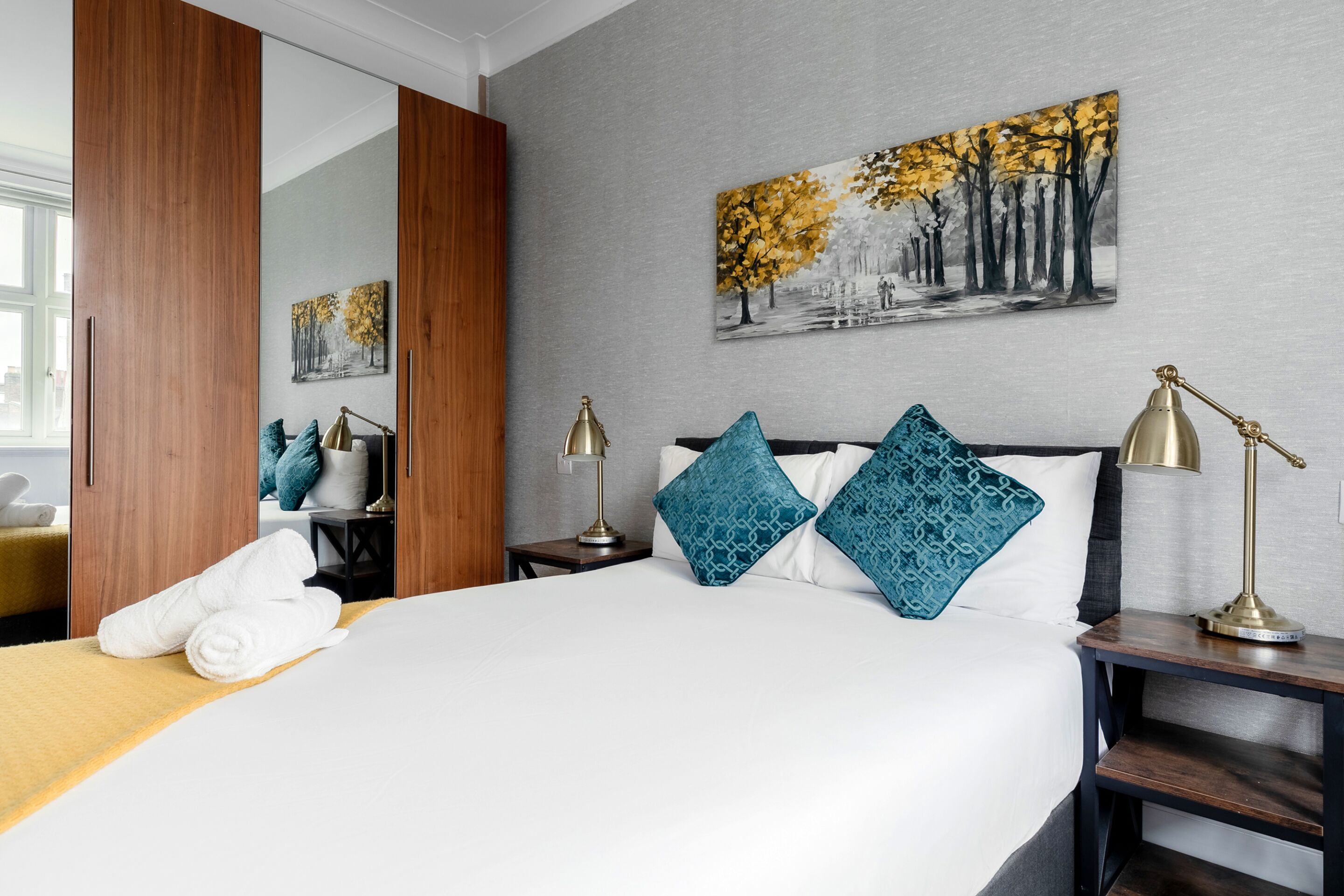 A hotel room with a large bed, two bedside lamps, a nightstand, a mirror, and artwork on the wall.