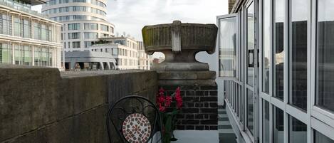 A balcony with a checkered floor, a round table with chairs, and a potted plant with flowers.