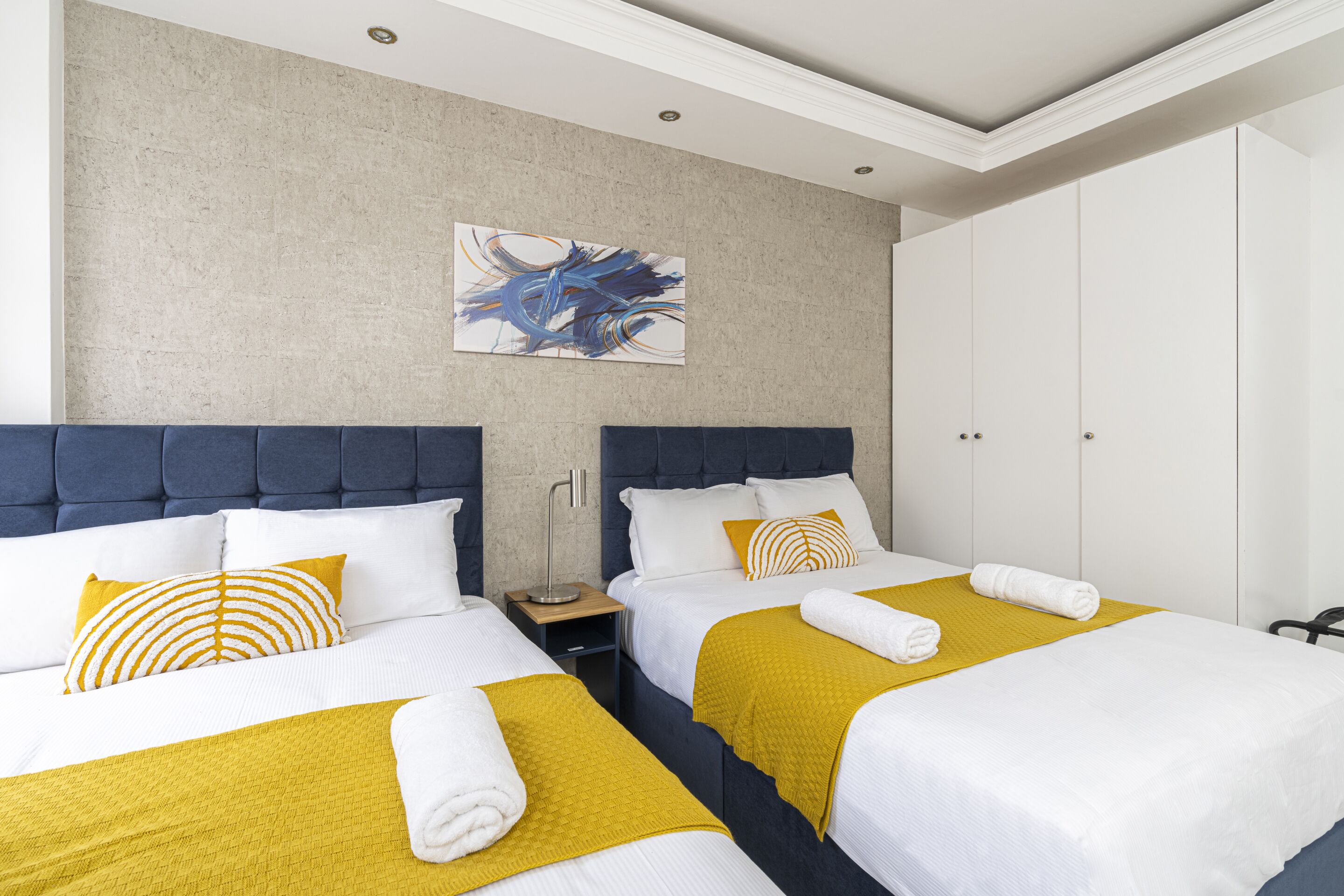 Habitación de hotel con dos camas, una mesita de noche, una lámpara, un cuadro y un armario.
